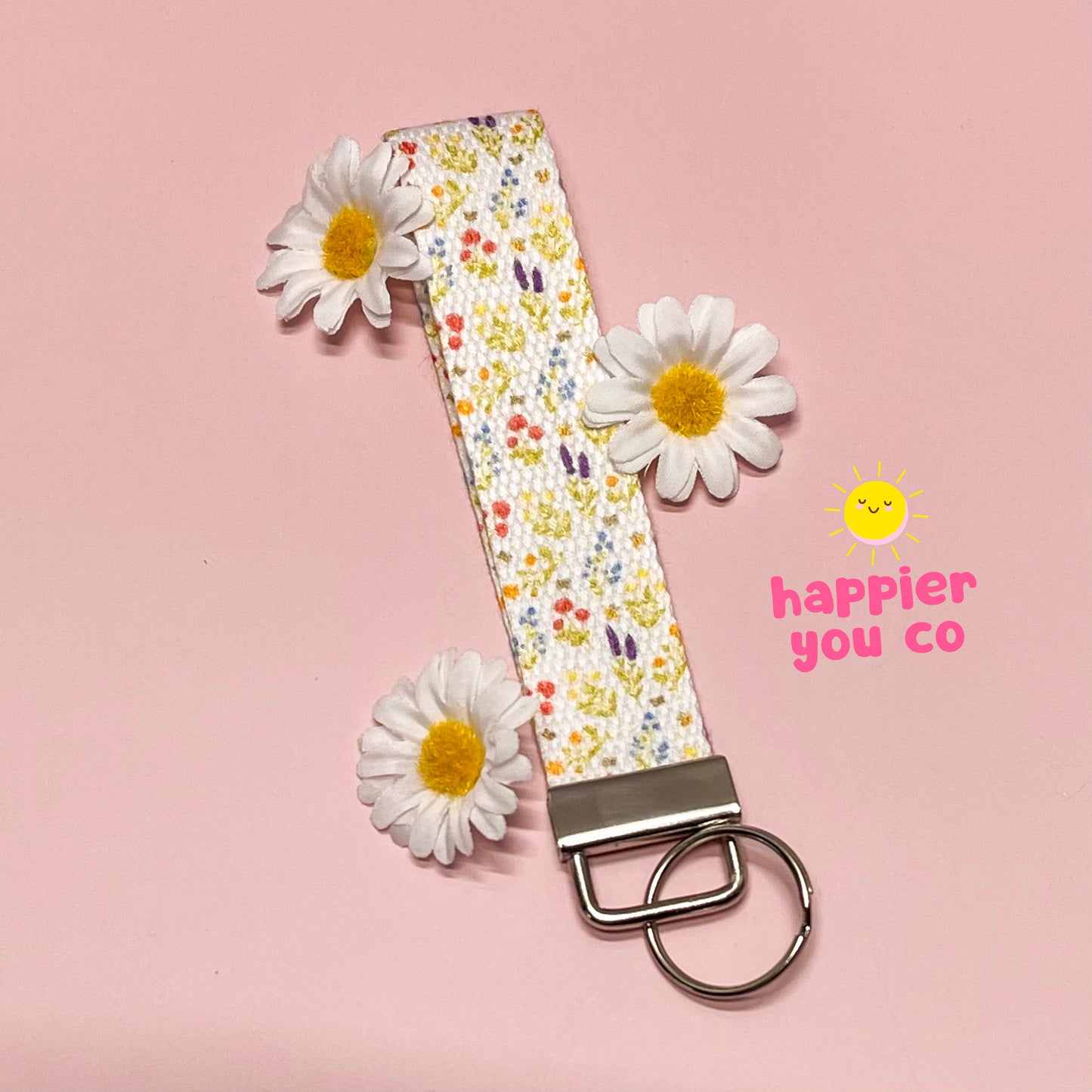 Floral patterned keychain with daisies on a pink background, featuring 'happier you co' branding.