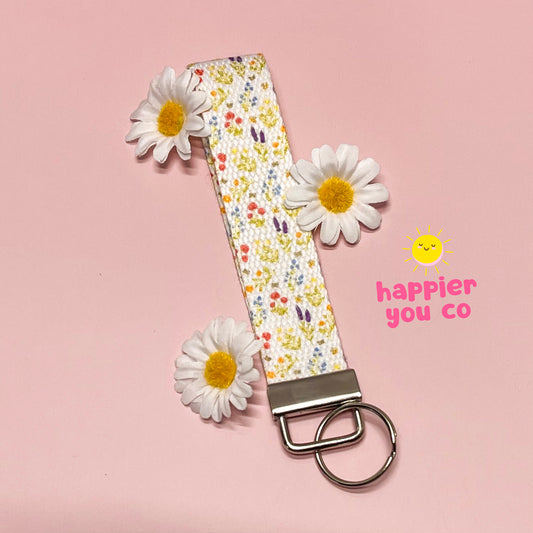 Floral patterned keychain with daisies on a pink background, featuring 'happier you co' branding.