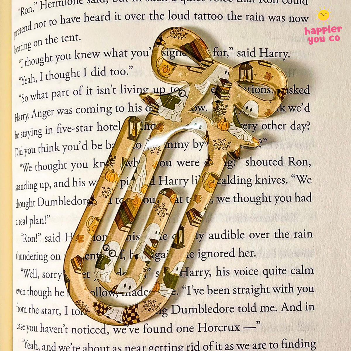 A decorative metal bookmark shaped like a pair of scissors, featuring a Harry Potter themed pattern with illustrations of Ron, Hermione, and Dumbledore, displayed on a page of book text.