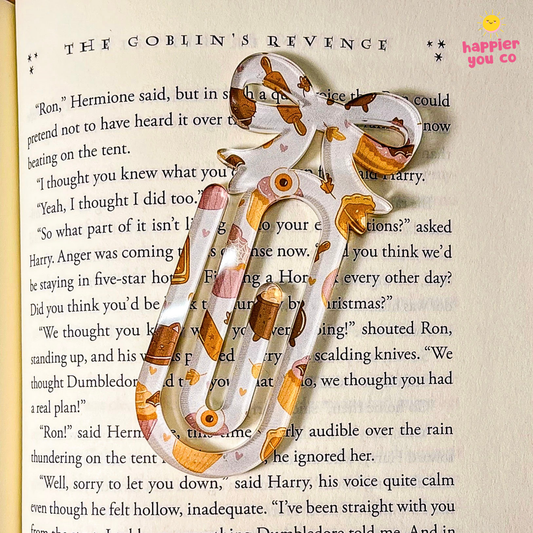 A decorative paper bookmark shaped like a bow and arrow, printed with a Halloween-themed pattern of orange, brown, and white, resting on an open book page.