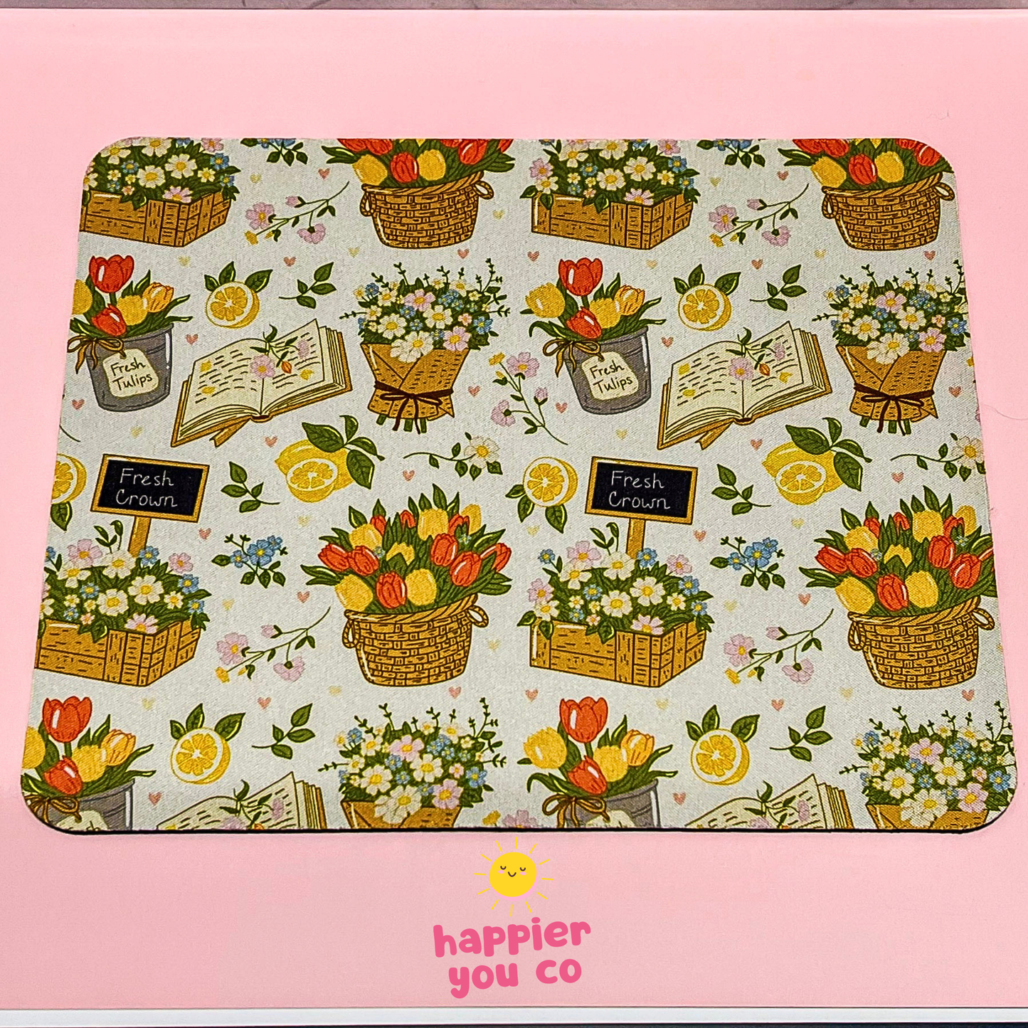 Decorative placemat with floral and fruit pattern on a pink background, featuring the 'happier you co' brand.