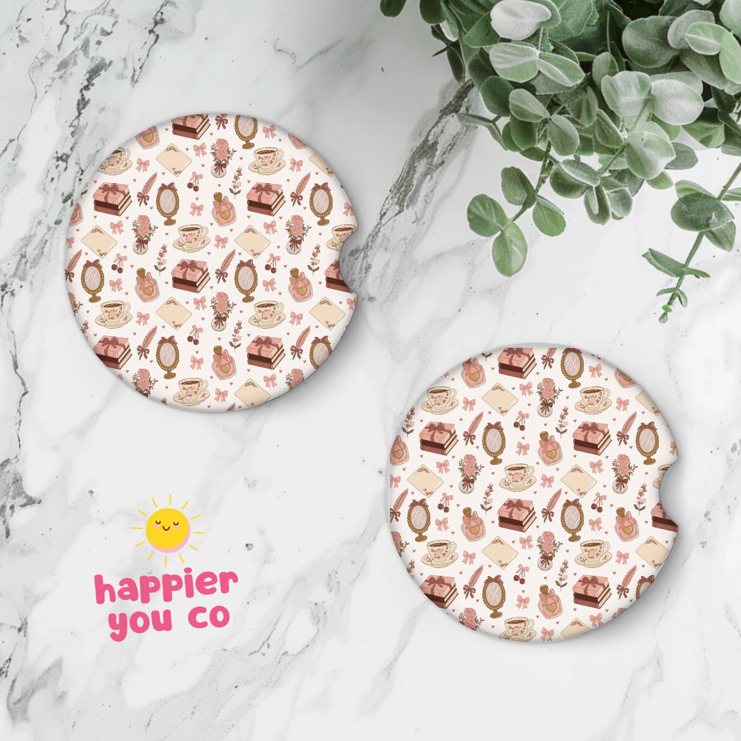 Two round coasters with a pattern of girly pink things on a marble surface with a plant.