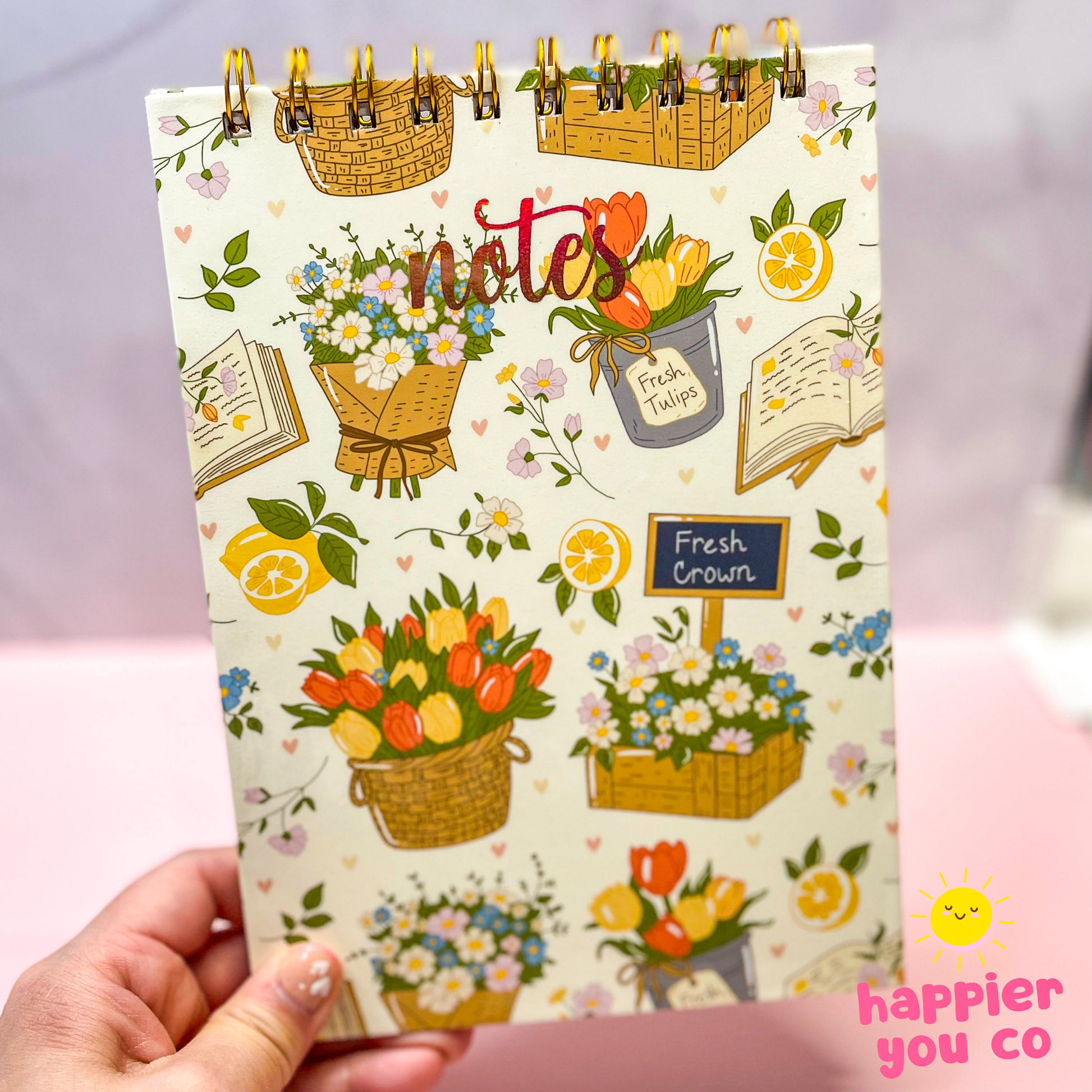 Notebook with floral design and 'notes' text held by a hand on a light pink background.