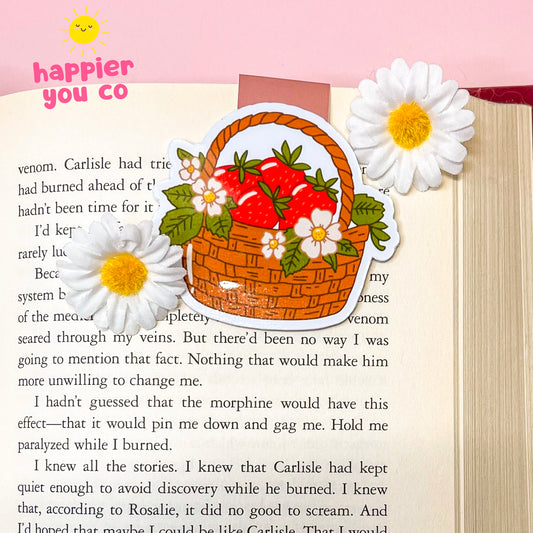 Decorative magnetic bookmark of a basket with strawberries and flowers on a book page with text.