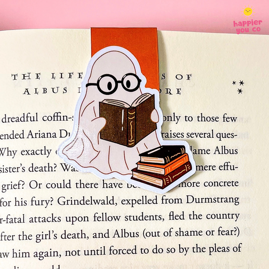 A ghost-shaped bookmark with round glasses and a book on its head, placed on an open book page with an orange bookmark tab behind it. The Happyer You Co logo appears in the top right corner.