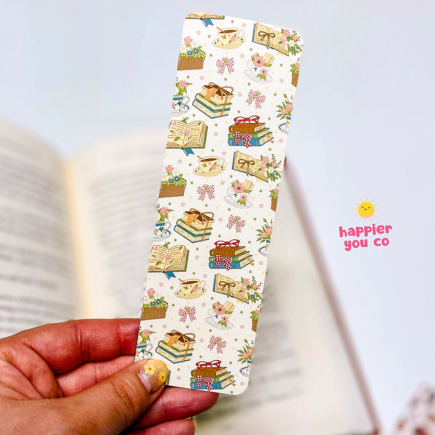 Decorative bookmark with illustrations held over an open book, featuring the brand 'happier you co'.