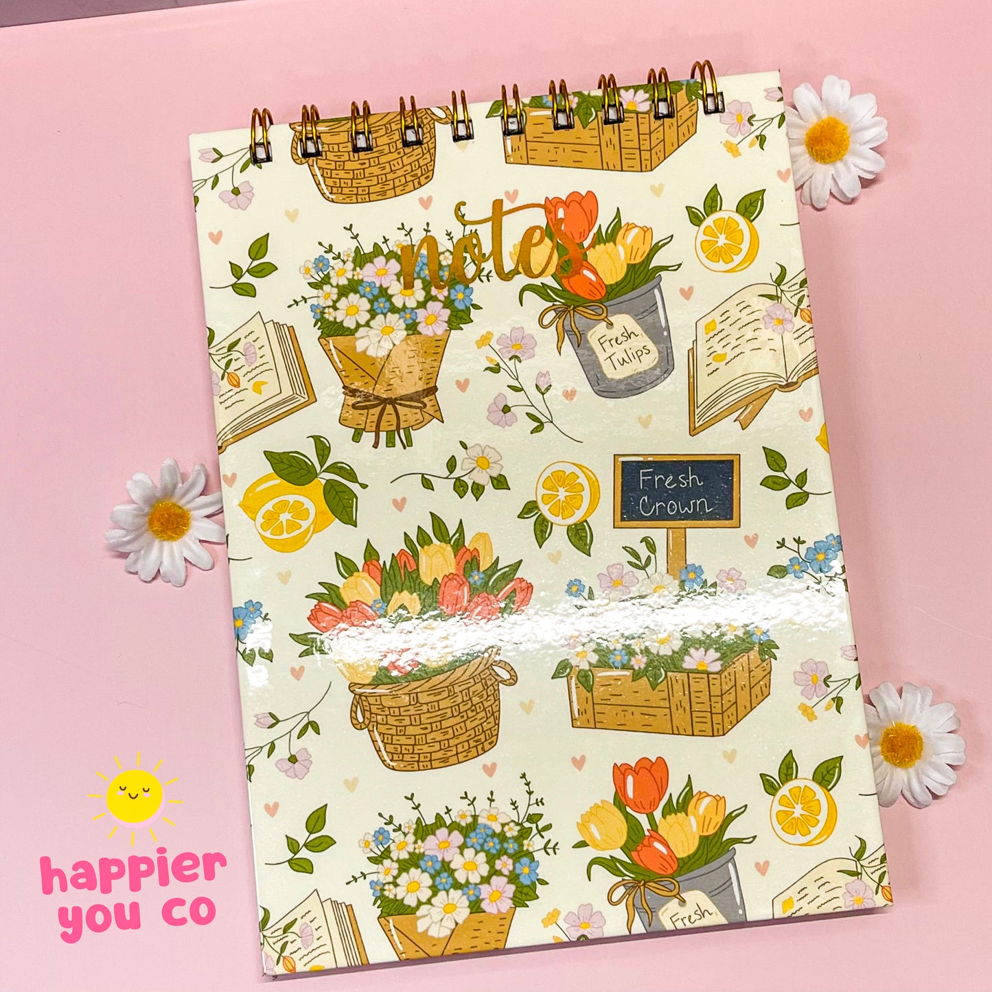 Notebook with floral and basket design on a pink background, featuring the brand 'happier you co'.