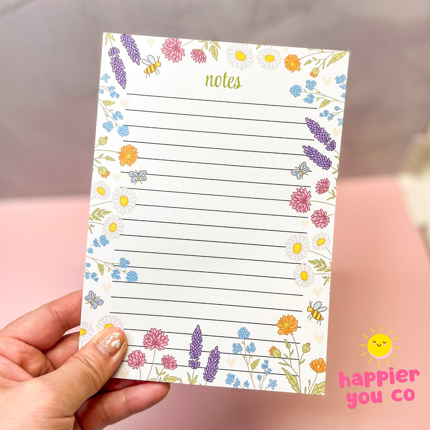 Floral notepad held by a hand with 'happier you co' branding.
