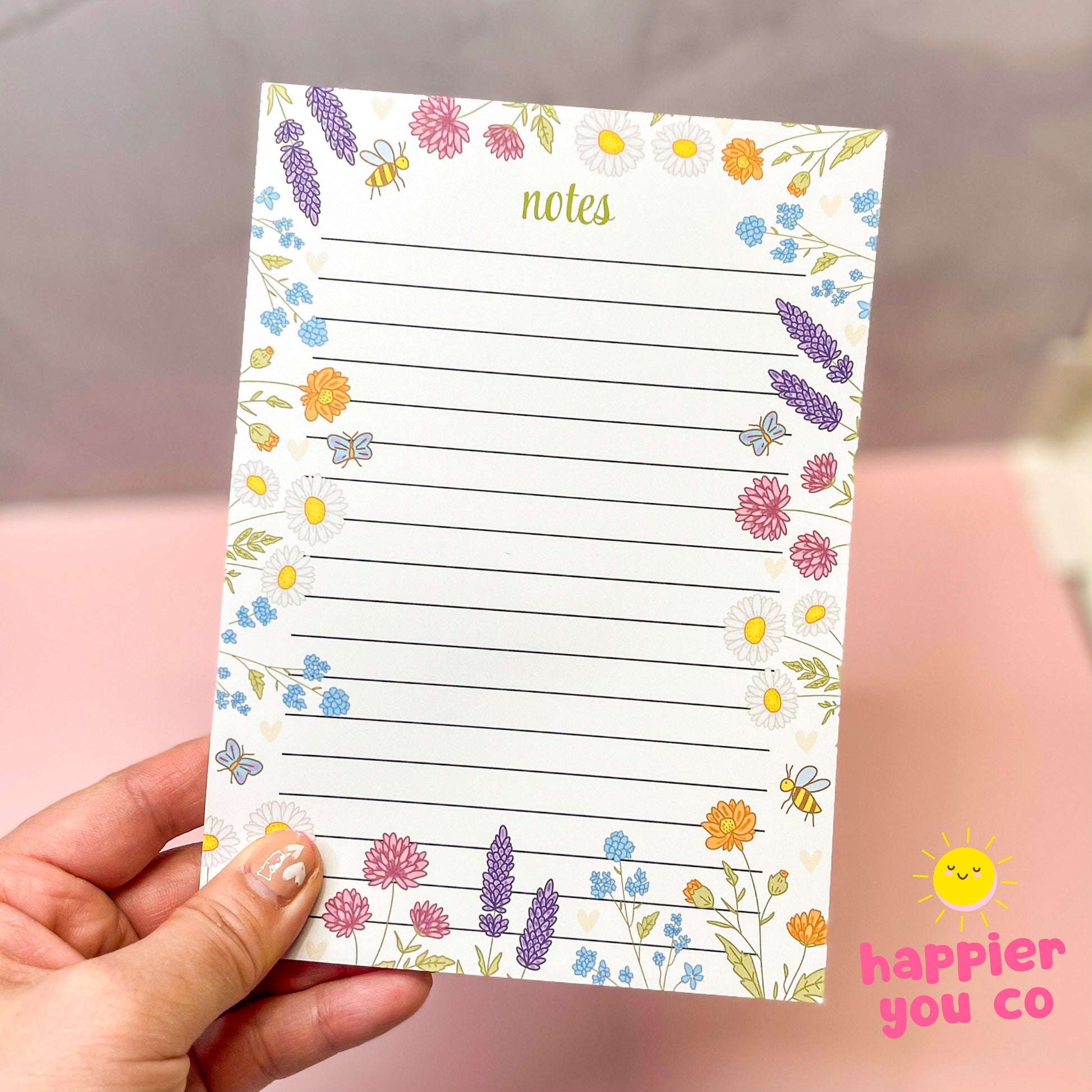 Floral notepad held by a hand with 'happier you co' branding.