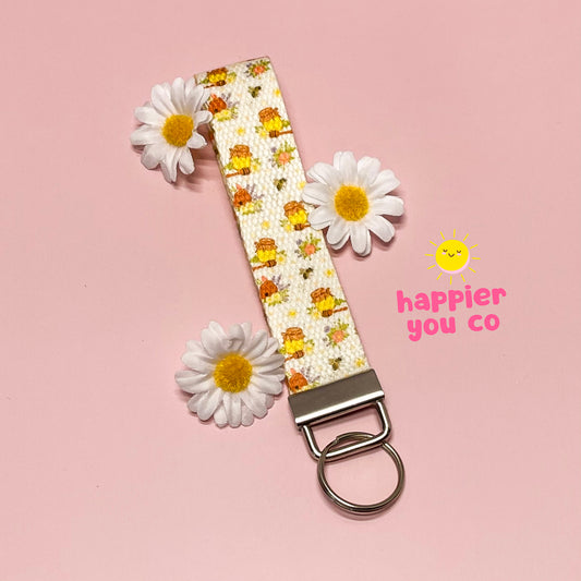 Keychain with floral design and 'happier you co' branding on a pink background