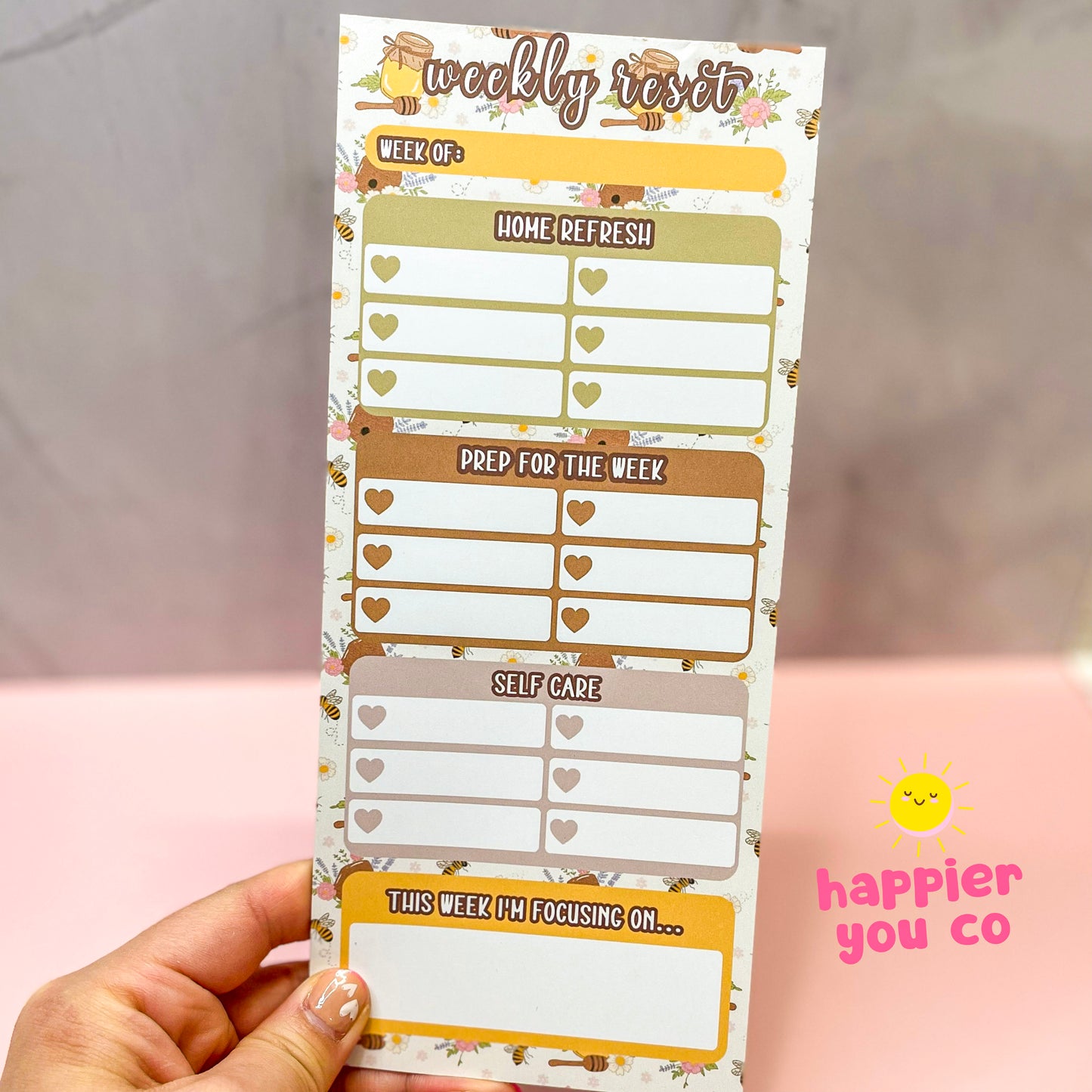 Weekly reset planner with a honey bee background held by a hand with a blurred background