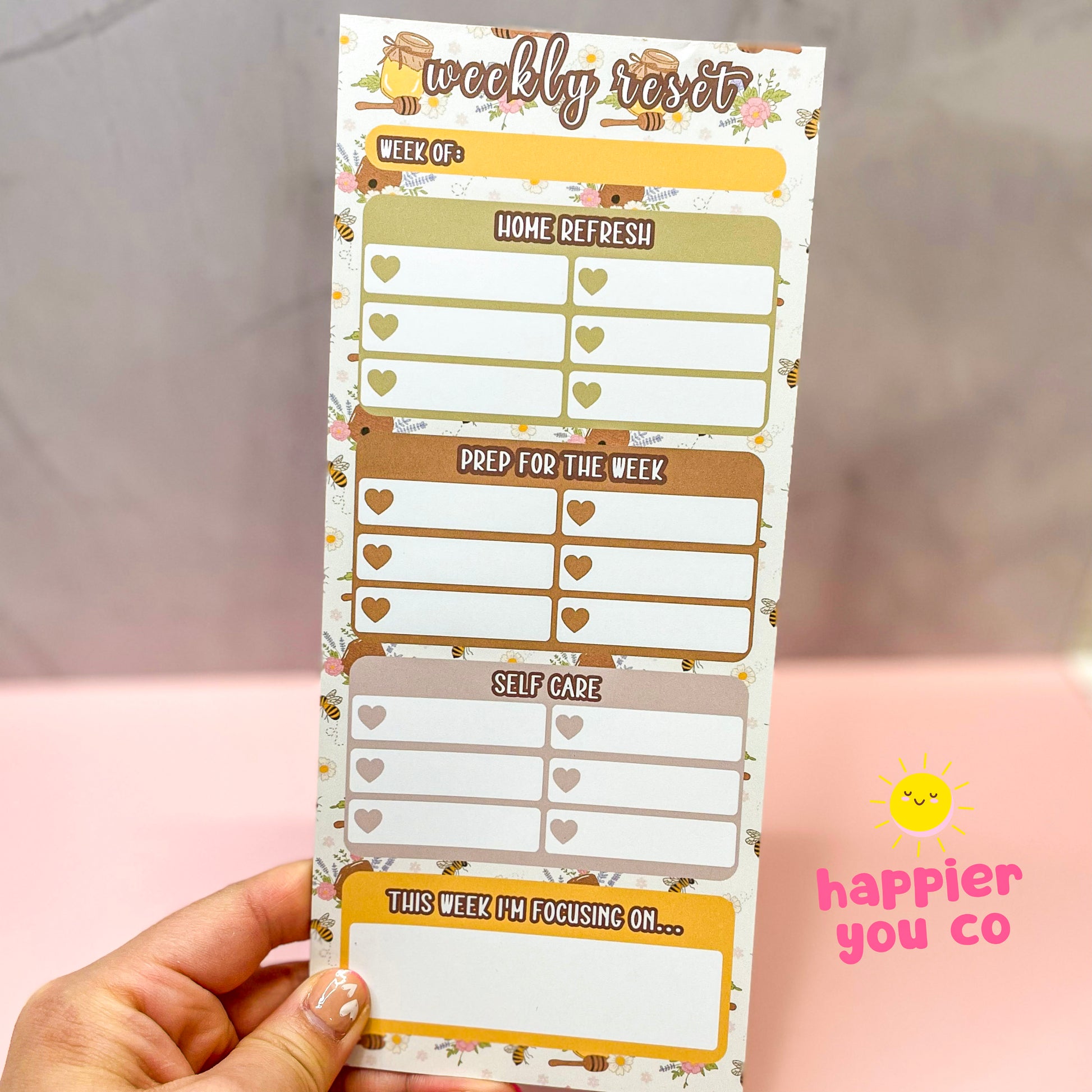 Weekly reset planner with a honey bee background held by a hand with a blurred background