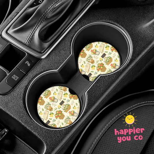 Two floral-patterned car coasters in a vehicle's cup holder with 'happier you co' branding.