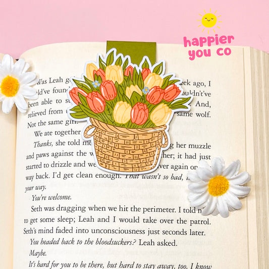 Floral bookmark with a basket of tulips on an open book, featuring the brand 'happier you co'.