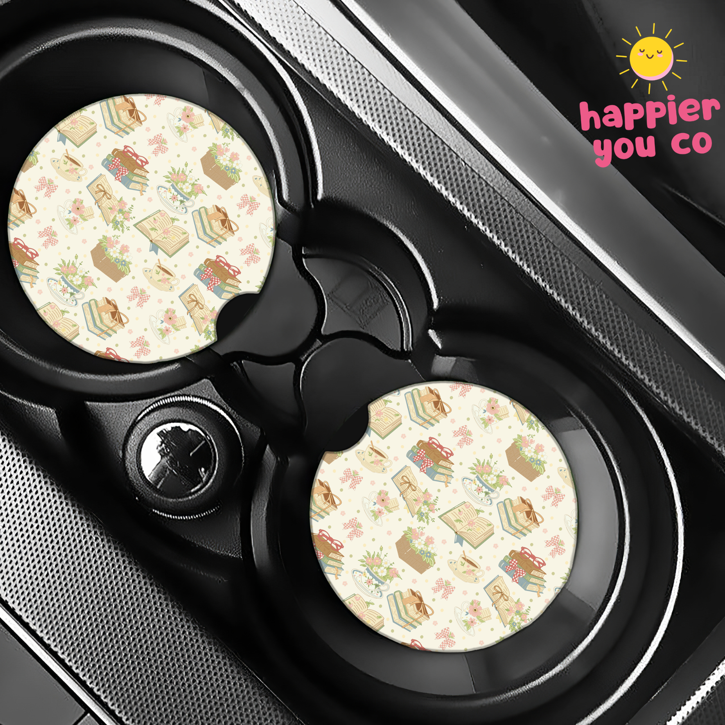 Two car coasters with a pattern of books and flowers on a cup holder tray, branded 'happier you co'.