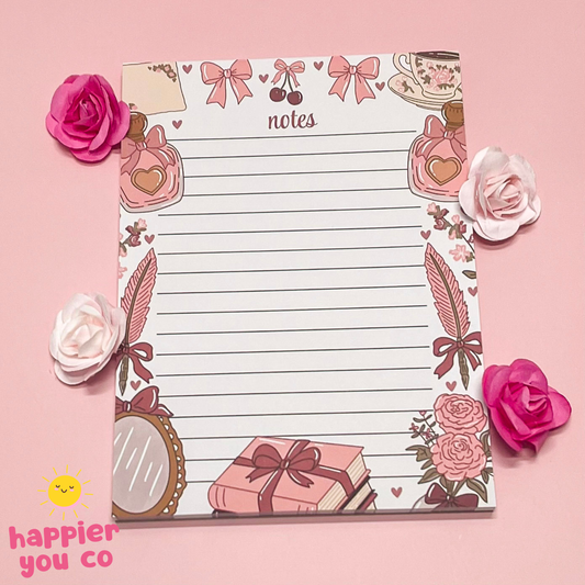 Decorative notepad with floral and gift designs on a pink background, featuring the brand 'happier you co'.