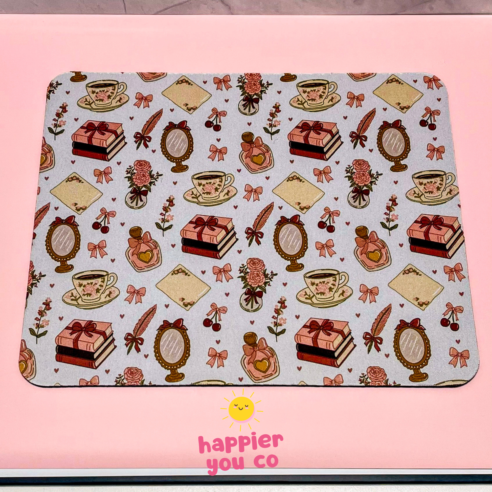 Decorative mouse pad with tea cups, cakes, and bows on a pink background with 'happier you co' branding.