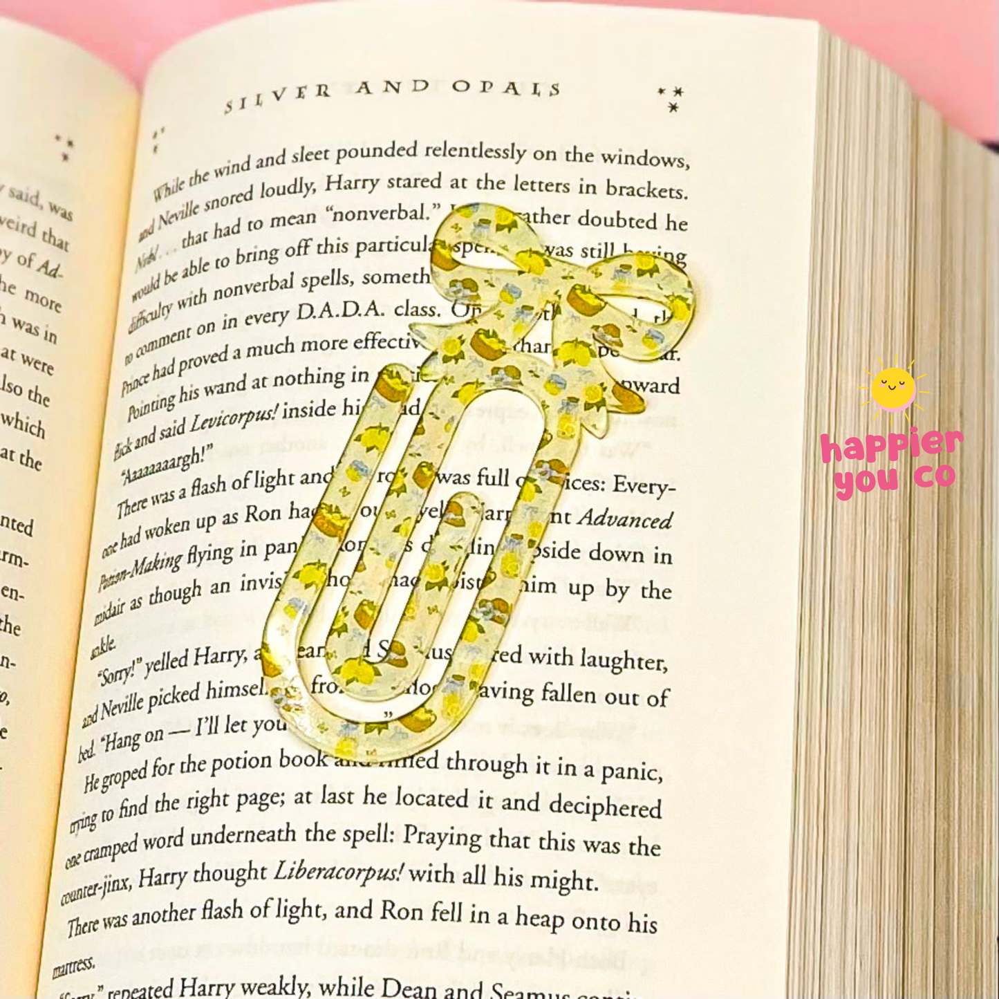 Floral-patterned paper clip on an open book with 'happier you co' branding.