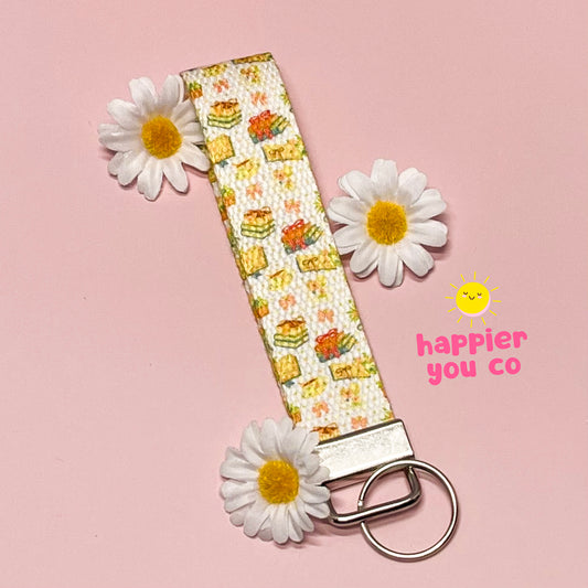 Keychain with floral pattern and daisies on a pink background, featuring the brand 'happier you co'.