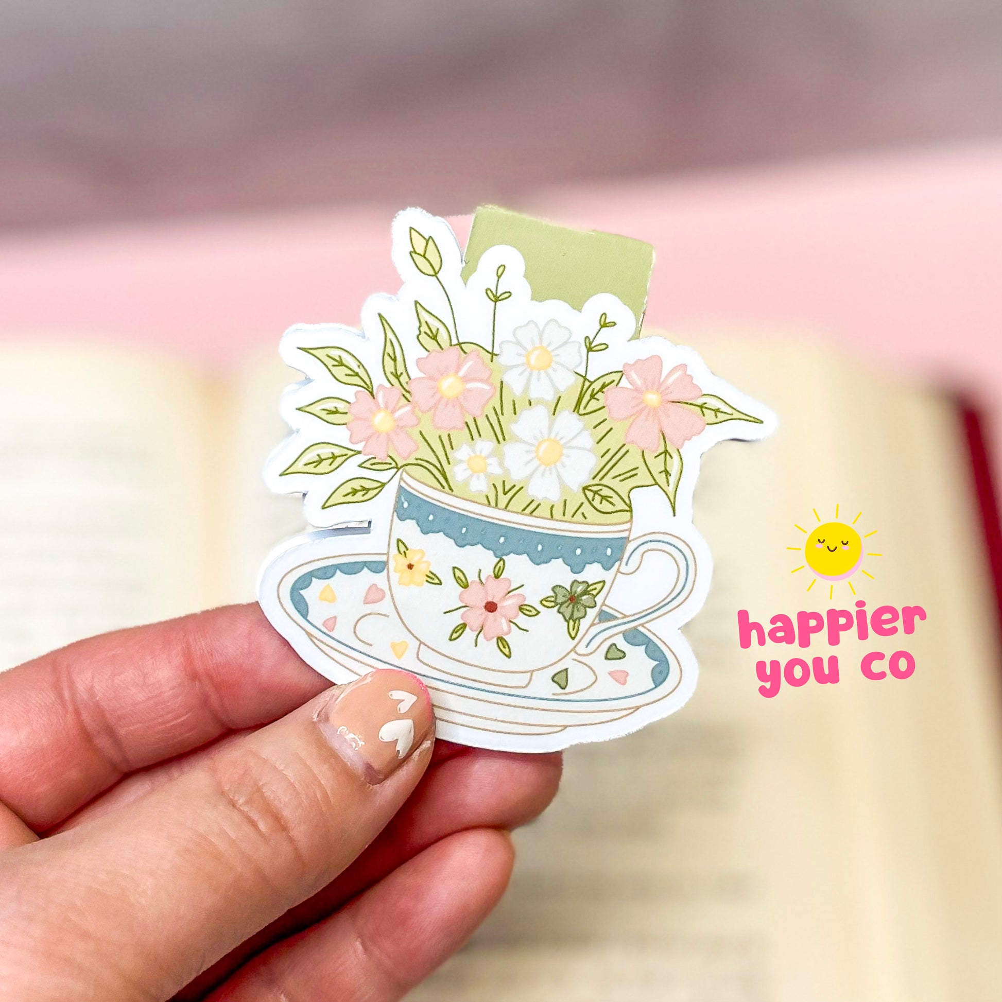 Magnetic bookmark of a teacup with flowers held by a hand against a blurred background