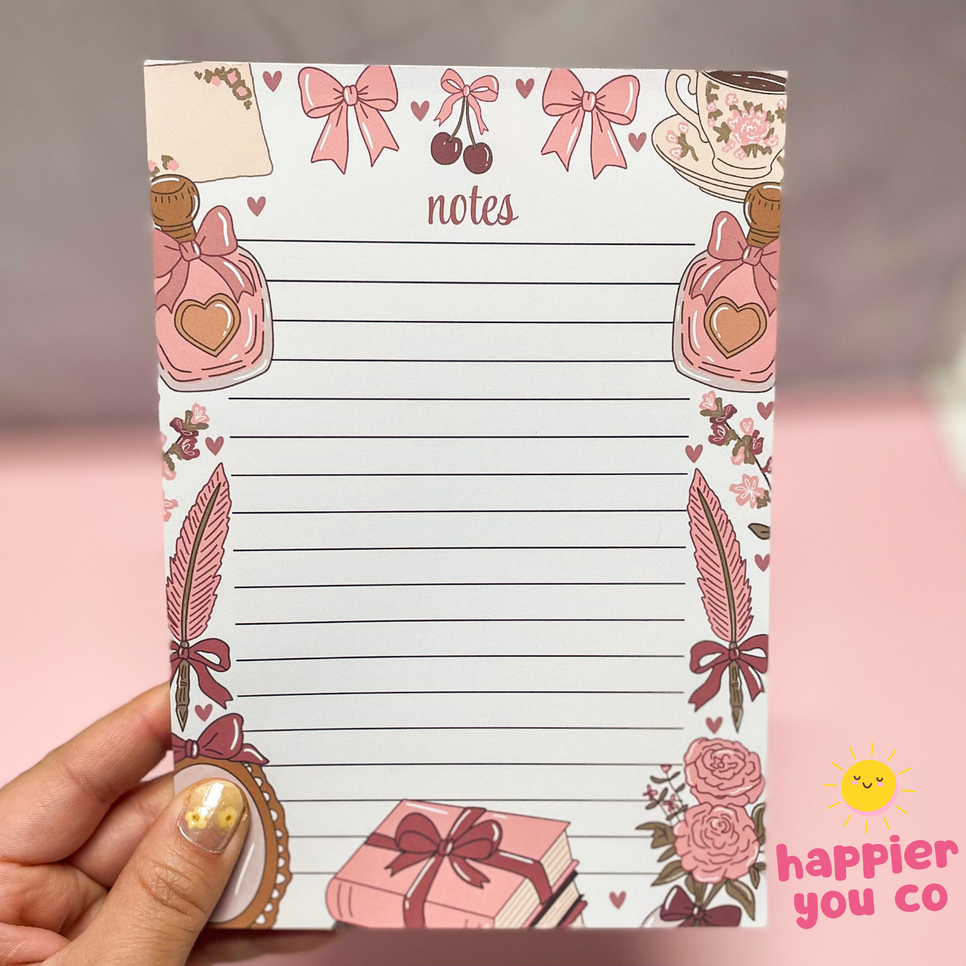 Notepad with decorative border held by a hand, featuring illustrations and the brand 'happier you co'.