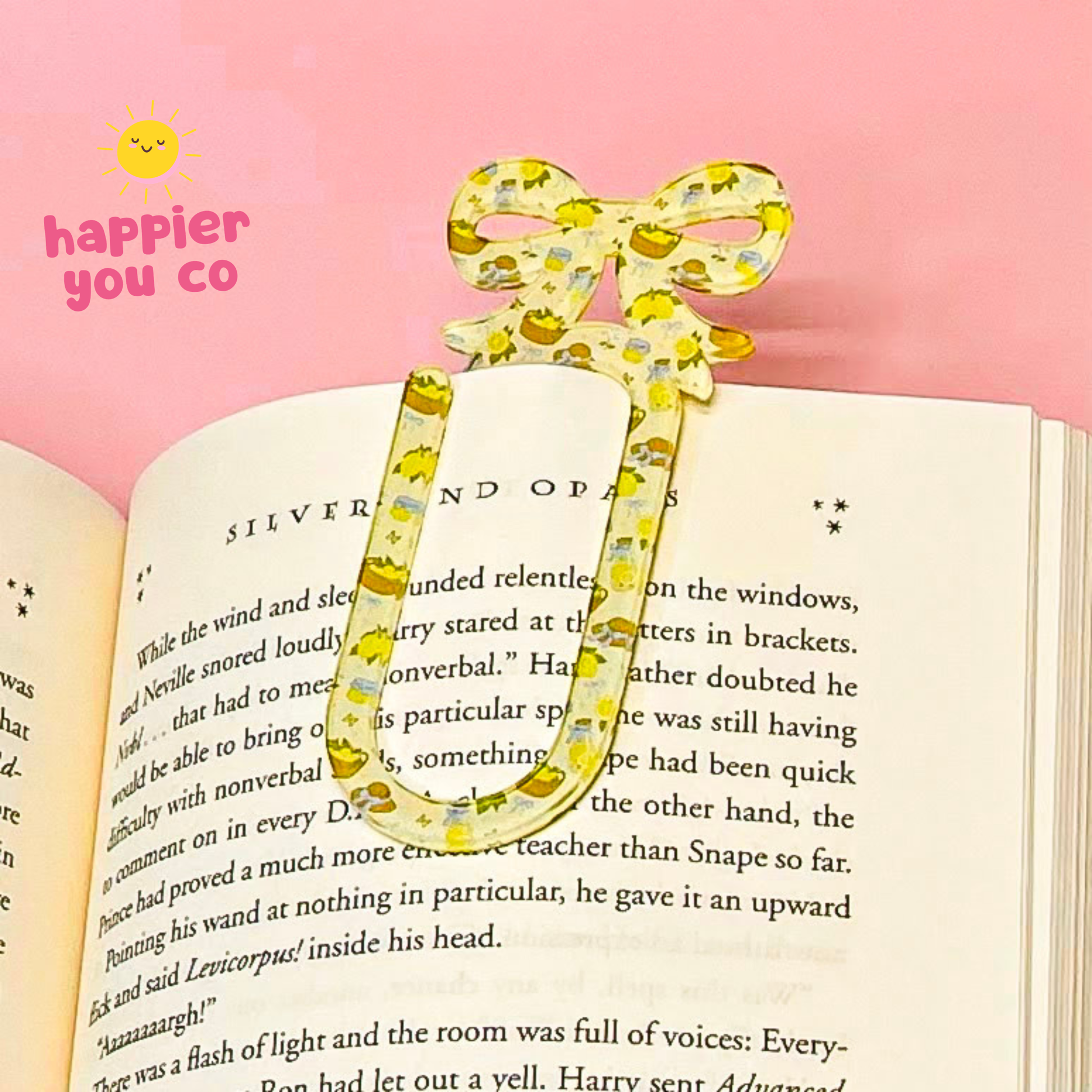Decorative yellow bow-shaped bookmark on an open book with 'happier you co' branding.
