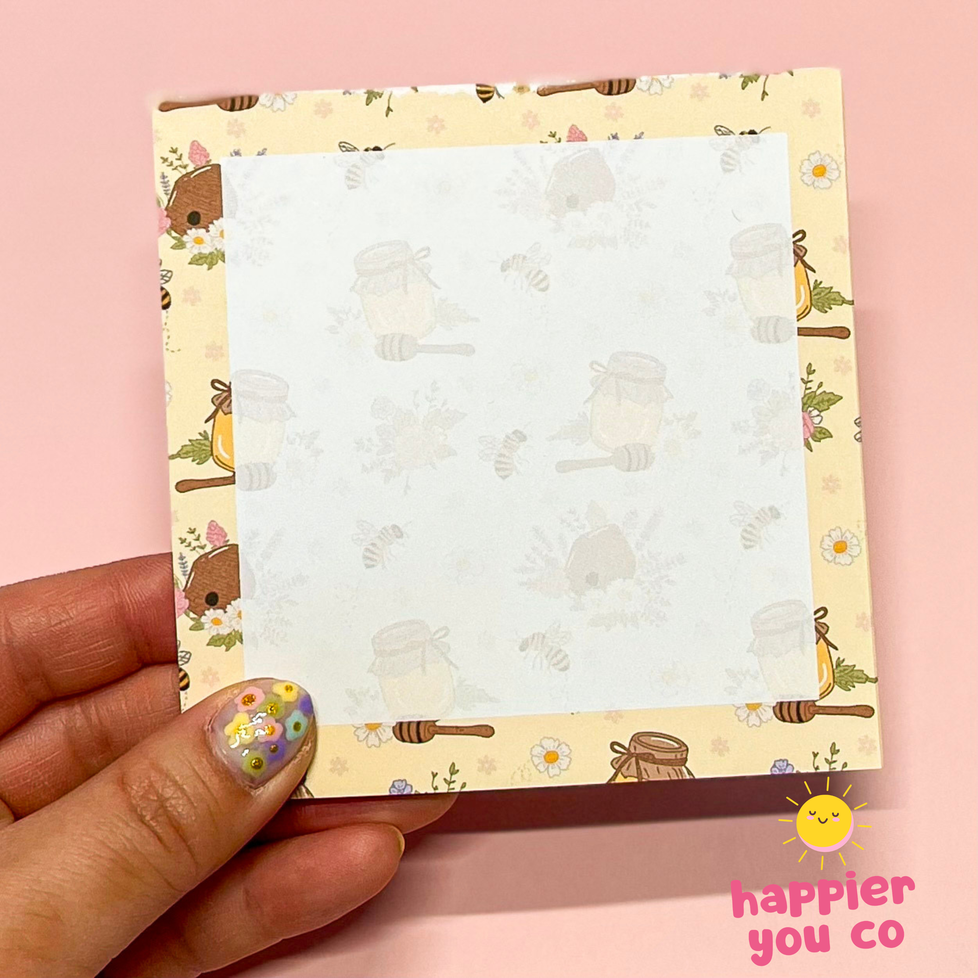 Small notepad with a floral design held by a hand on a pink background, with 'happier you co' branding.