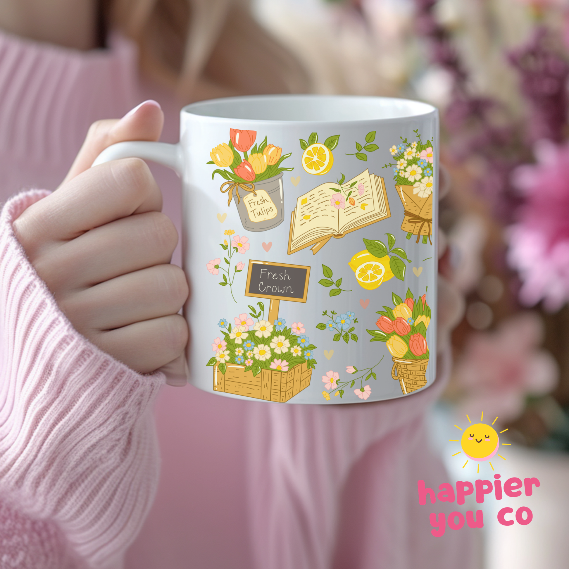 Person holding a mug with floral illustrations and 'happier you co' branding.