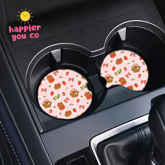 Two pink car coasters with strawberry pattern on a car cup holder, featuring 'happier you co' logo.