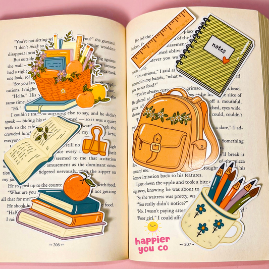A set of colorful school-themed stickers arranged on the pages of an open book. The stickers include a pencil case with flowers, a notebook with a ruler, a backpack, a pencil holder with flowers, a paint palette, and other school accessories, all styled on a pink background.