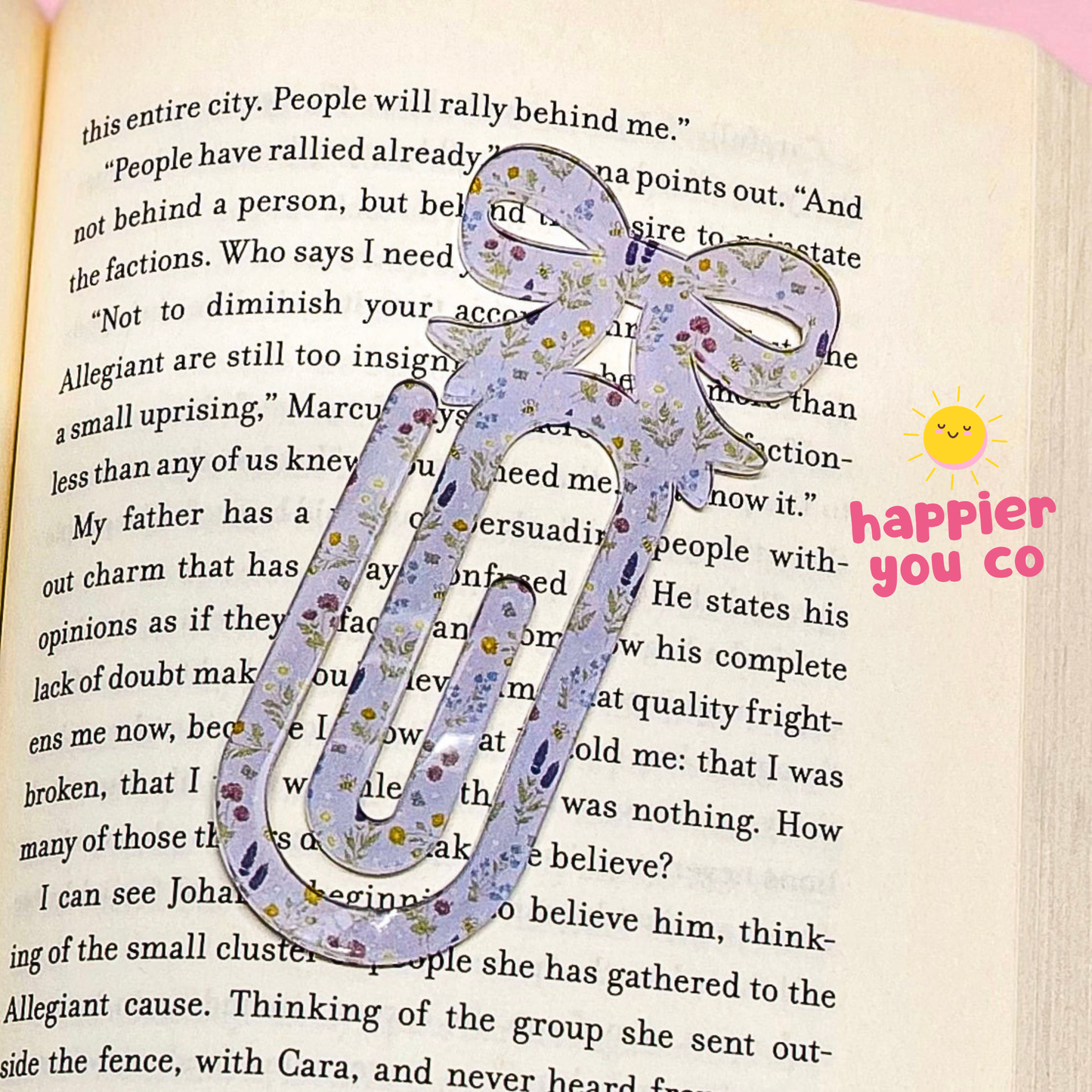Decorative floral bow paperclip on an open book with 'happier you co' branding.